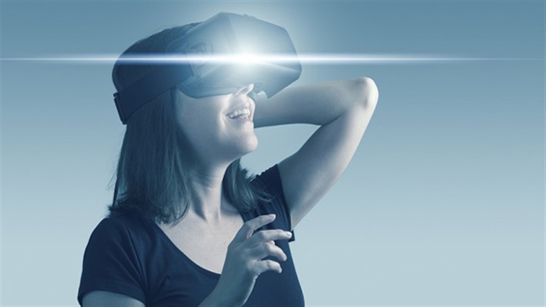 A mid-adult woman wears a virtual reality headset, controlling the experience with hand gestures. There is a horizontal streak of light lens flare from the VR headset. Blue-toned image.