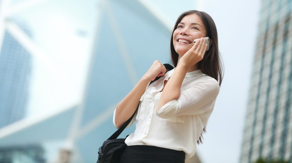 Business woman talking on smart phone in Hong Kong. Asian business people office worker talking on smartphone smiling happy. Young multiracial Chinese Asian / Caucasian female professional outside.