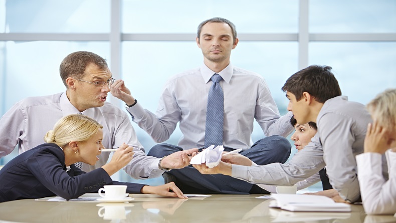 Furious arguing business team and CEO meditating in lotus position on the table