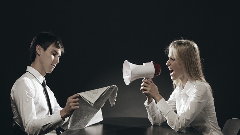 Girl with megaphone, shouting loudly, young man is reading a newspaper ignoring her